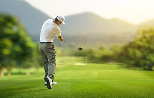 Golfer teeing off on a lush golf course with mountain scenery in the background during a sunny day, following through on a powerful drive.